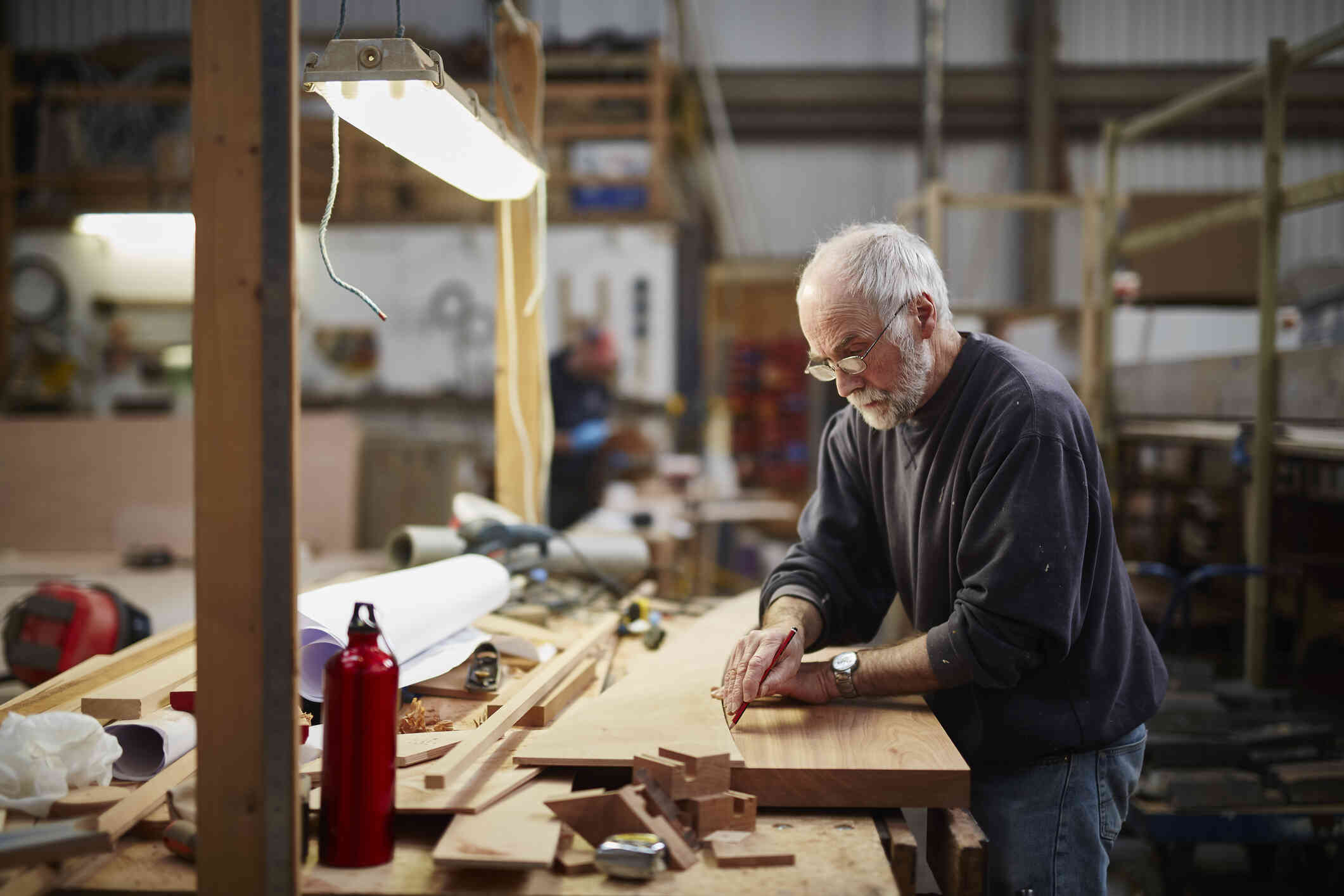 A mature man stands in his workshop and works art a wood crafting project with a serious expression.